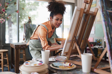 Beautiful american african artist woman painting in art studio at the university classroom