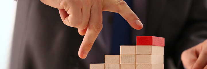Man hand raises fingers up a wooden staircase made of wooden blocks. Successful career leader and achievement of business goals