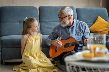 Granddad singing and playing guitar for his little granddaughter in their living room