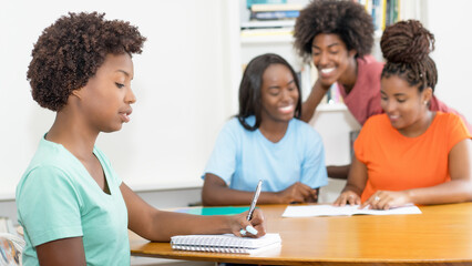 Working black female student at desk with group of learning african american students