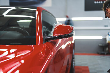 Front view of car detailing process. Specialist using PPF to cover red paint of a sports car....
