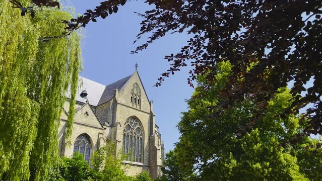 Static shot of the Dutch Abbes Church in Thorn with a view of the architecture while the trees blow in the wind on a sunny cloudless day