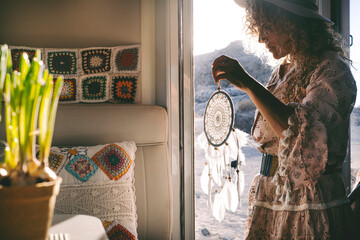 Wanderlust lifestyle people. One woman holding dreamcather decoration on the door of her mobile home with outdoors and sunset time outside. Concept of vanlife and freedom. Happy life independent woman