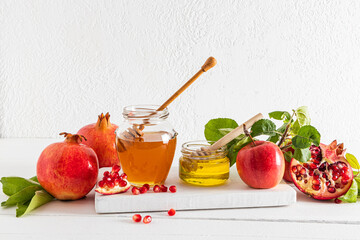 Front view of two cans of honey, ripe pomegranates and apples on a white wooden podium board. Traditional New Year's treat for Roshashan.