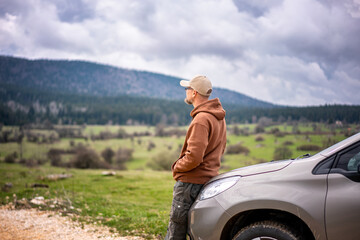 Fototapeta na wymiar Adult caucasian middle aged male traveler standing next to the car and admiring the mountain