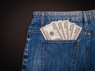 Five 100 US dollar banknotes in a jeans pocket on a black background.