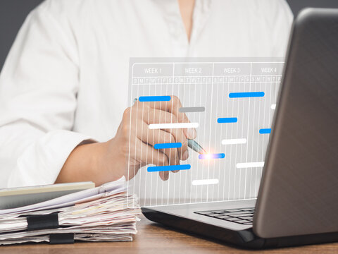 Project manager working on a laptop and updating tasks and milestones progress planning with a Gantt chart scheduling interface on a virtual screen.