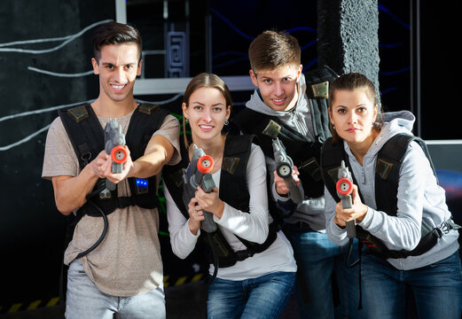 Portrait of smiling young friends with laser guns during lasertag game in dark room