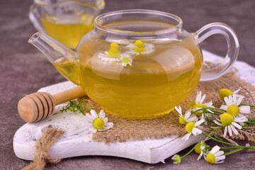 Healing sai from chamomile with honey in a transparent teapot.
