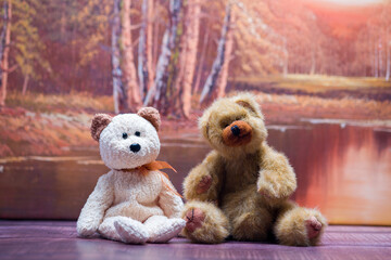 Small Brown and Beige  Teddy bear sitting on a bench with an autumn scene in the back ground.