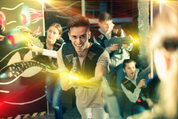 Obraz na płótnie Canvas Portrait of happy young man with laser pistol and playing laser tag with his friends in dark room. High quality photo