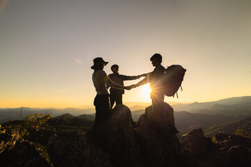 Silhouette of celebrating life, Hikers climbing up mountain cliff. Businessman and women group hike on the peak of  rocks mountain at sunset, success, winner and leader concept.