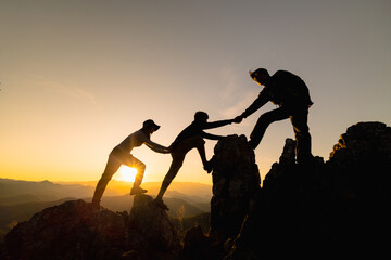 Silhouette of  Hikers climbing up mountain cliff. Climbing group helping each other while climbing up in sunset. Concept of help and teamwork.