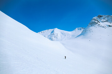 Wide open shot of lonely figure of man walk up mountain slope during mountaineering adventure hike or ski tour. Outdoors winter activity in wilderness