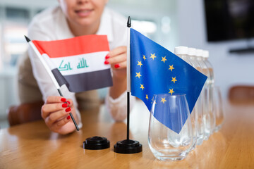 Employee of delegation prepares negotiating table - sets up the flag of European Union and Iraq