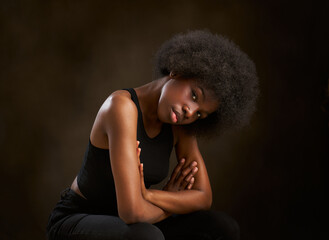 Happy young ethnic girl with afro hairstyle sitting with arms folded