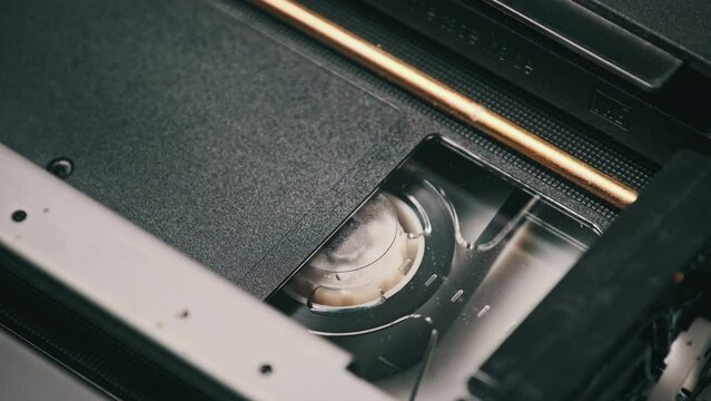 VHS video tape putting inside a VCR recorder and plays. Vintage VHS mechanism of videotape insert tape to video head. Retro videotape rotates in a video cassette. Playing an old movie, broadcasting.
