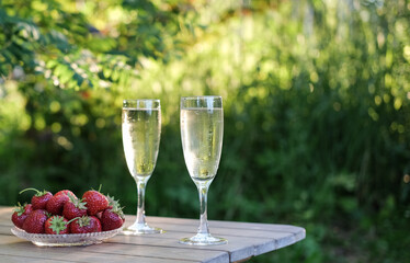 Glasses of champagne and strawberries on a table in a summer garden against the backdrop of evening sunlight