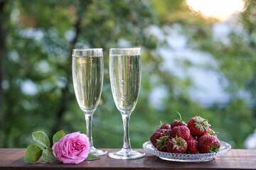 Glasses of champagne and strawberries on a terrace in a summer garden against the backdrop of evening sunlight
