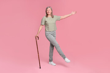 Senior woman with walking cane posing on pink background