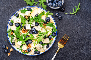 Gourmet salad with sweet pears, blueberries, blue cheese, arugula and walnuts. Black table background, top view