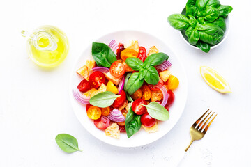 Panzanella summer vegetable salad with stale bread, colorful tomatoes, red onion, olive oil, salt and green basil, white table background, top view