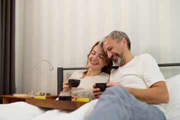 Mature couple enjoying coffee and breakfast at home in bed