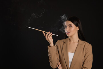 Fototapeta premium Woman using long cigarette holder for smoking on black background, space for text