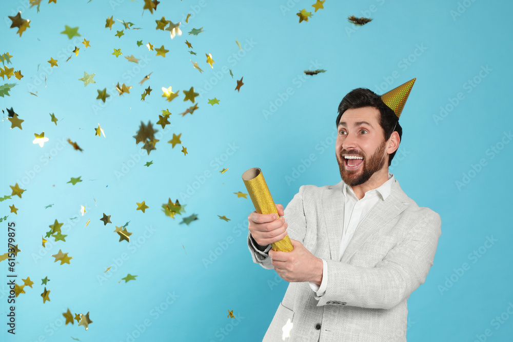 Wall mural Emotional man blowing up party popper on light blue background