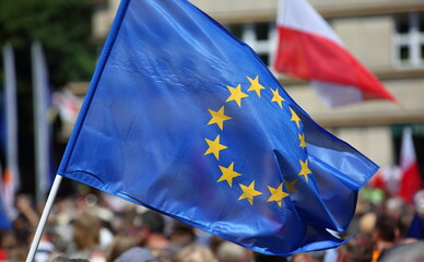 european union flag, in background flag of Poland, crowd of people while demonstrate to support democracy