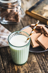 Glass of milk with striped straw on wooden table.