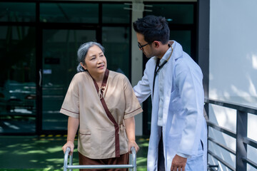 Obraz premium Asian elderly woman walking with walker under close supervision of physiotherapist in rehab center