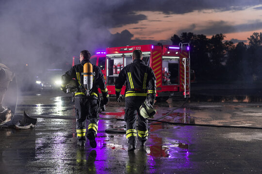 Brave Firefighters Team Walking to the Camera. In Background Paramedics and Firemen Rescue Team Fight Fire in Car Accident, Insurance and Save Peoples Lives concept.