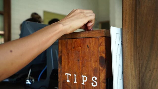 Woman tipping a restaurant, inserting a paper bill in a box assigned for tips