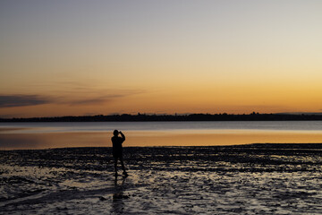 silhouette of a person taking pictures on the beach at sunset