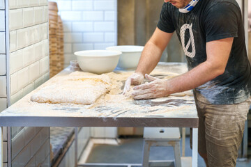 A close-up photo in a bakery shows an unidentified young man meticulously kneading wheat dough,...