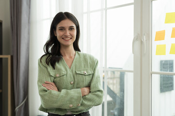 Portrait of happy young business woman standing with crossed arms in office. Business people and office concept