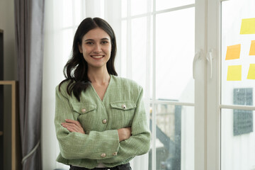 Portrait of happy young business woman standing with crossed arms in office. Business people and...