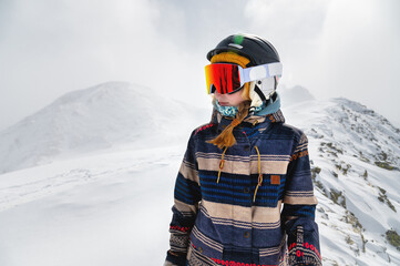Skier, skiing, winter sports, female skier portrait. A beautiful girl stands against the backdrop of snow-capped mountains and looks to the side, freeride