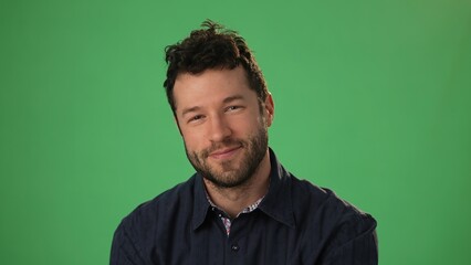 Handsome dreamful bearded young guy 20s in hoodie isolated on green screen chroma key background in studio. People sincere emotions, lifestyle concept. Smiling looking at the camera.