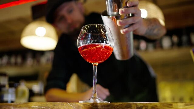 A professional bartender is preparing an alcoholic cocktail with ice cubes to customers at the bar or disco club. Close up of a professional bartender is mixing an alcoholic cocktail with professional