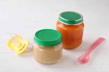 Jars with healthy baby food, spoon and pacifier on white wooden table