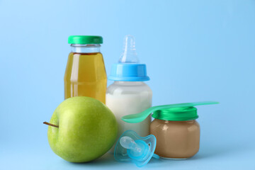 Healthy baby food, juice, milk, apple, spoon and pacifier on light blue background