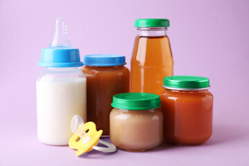 Healthy baby food, juice, milk and pacifier on lilac background