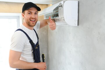 Smiling young male electrician repair conditioner in client home. Man mechanic or repairman fix filters in air condition device at customer house