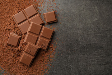 Delicious milk chocolate and cocoa powder on grey table, flat lay. Space for text