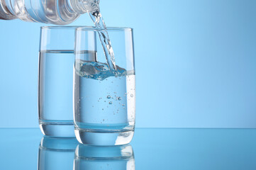 Pouring water from bottle into glass on light blue background. Space for text