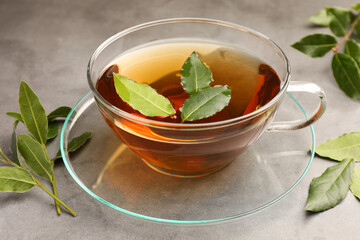 Cup of freshly brewed tea with bay leaves on grey table, closeup