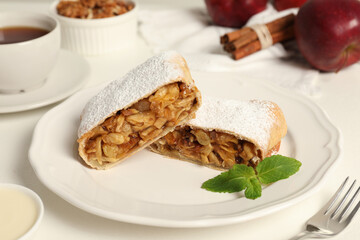 Delicious strudel with apples, nuts and raisins on white table, closeup