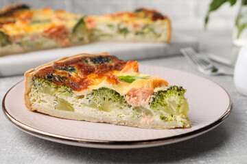Piece of delicious homemade quiche with salmon and broccoli on light grey table, closeup